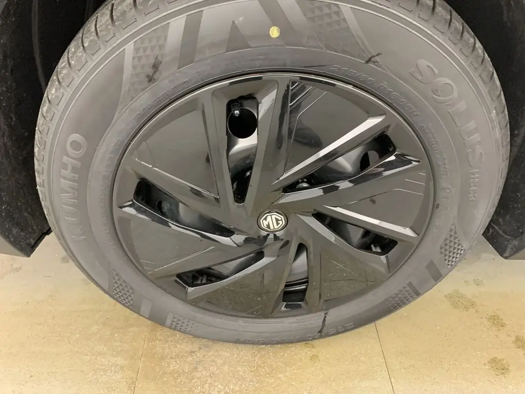 Gros plan sur la jante noire brillante avec logo MG au centre du MG ZS blanc Dover White, roue avant droite visible.