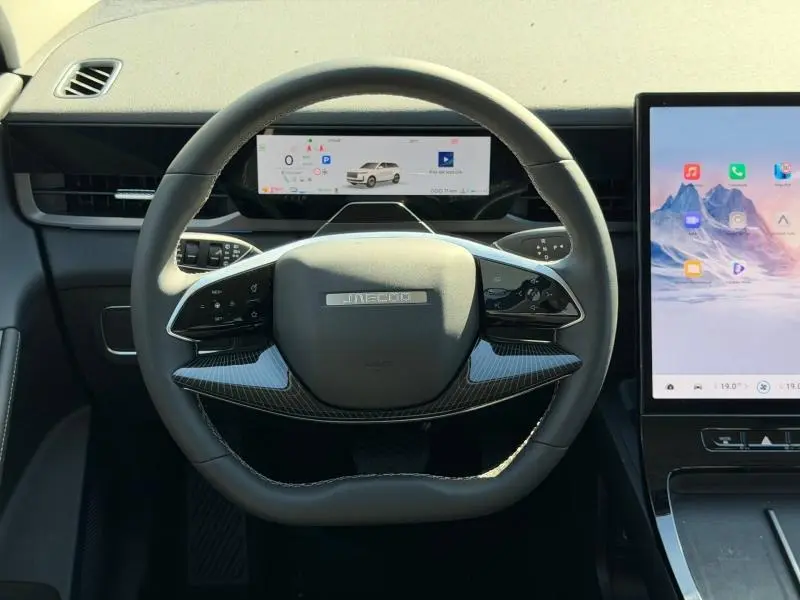 Vue frontale du volant noir avec insert carbone du JAECOO J5, écran numérique et large écran tactile latéral visible.