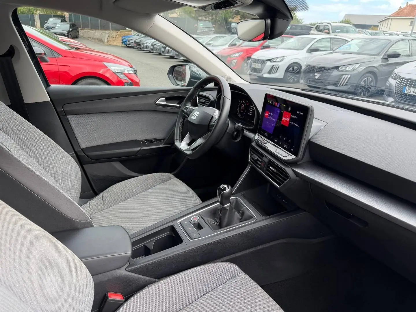 Vue intérieure côté conducteur du SEAT Leon 2025 gris, volant cuir multifonction et écran tactile central visible.