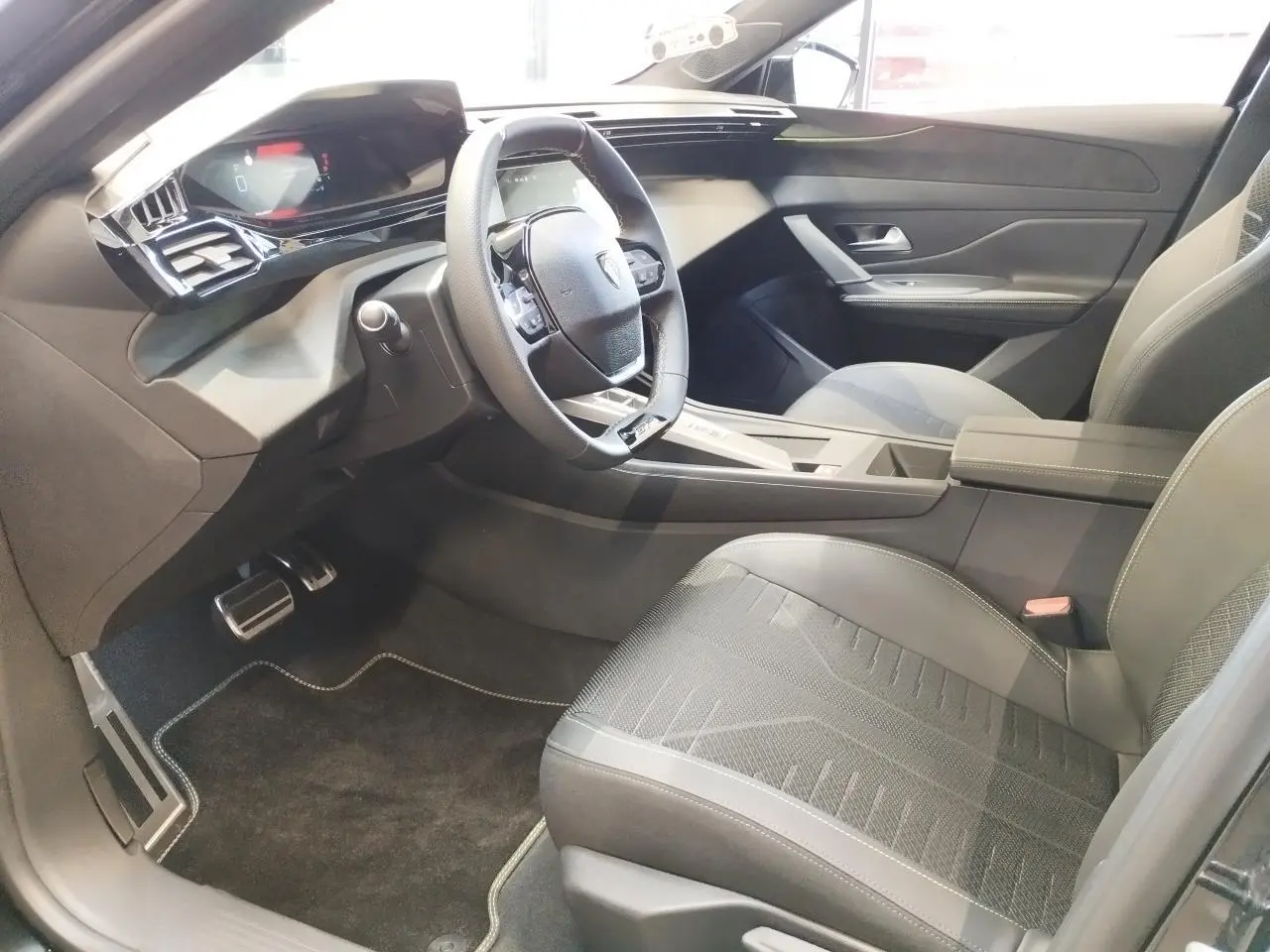 Intérieur avant droit de la Peugeot 308 1.2i Hybrid 2026 avec sellerie noire et volant compact GT cuir.