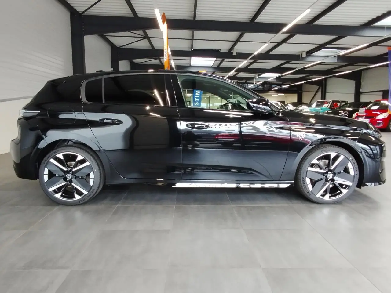 Vue de profil côté gauche d'une Peugeot 308 noire métallisée avec jantes alliage bi-tons dans un showroom.