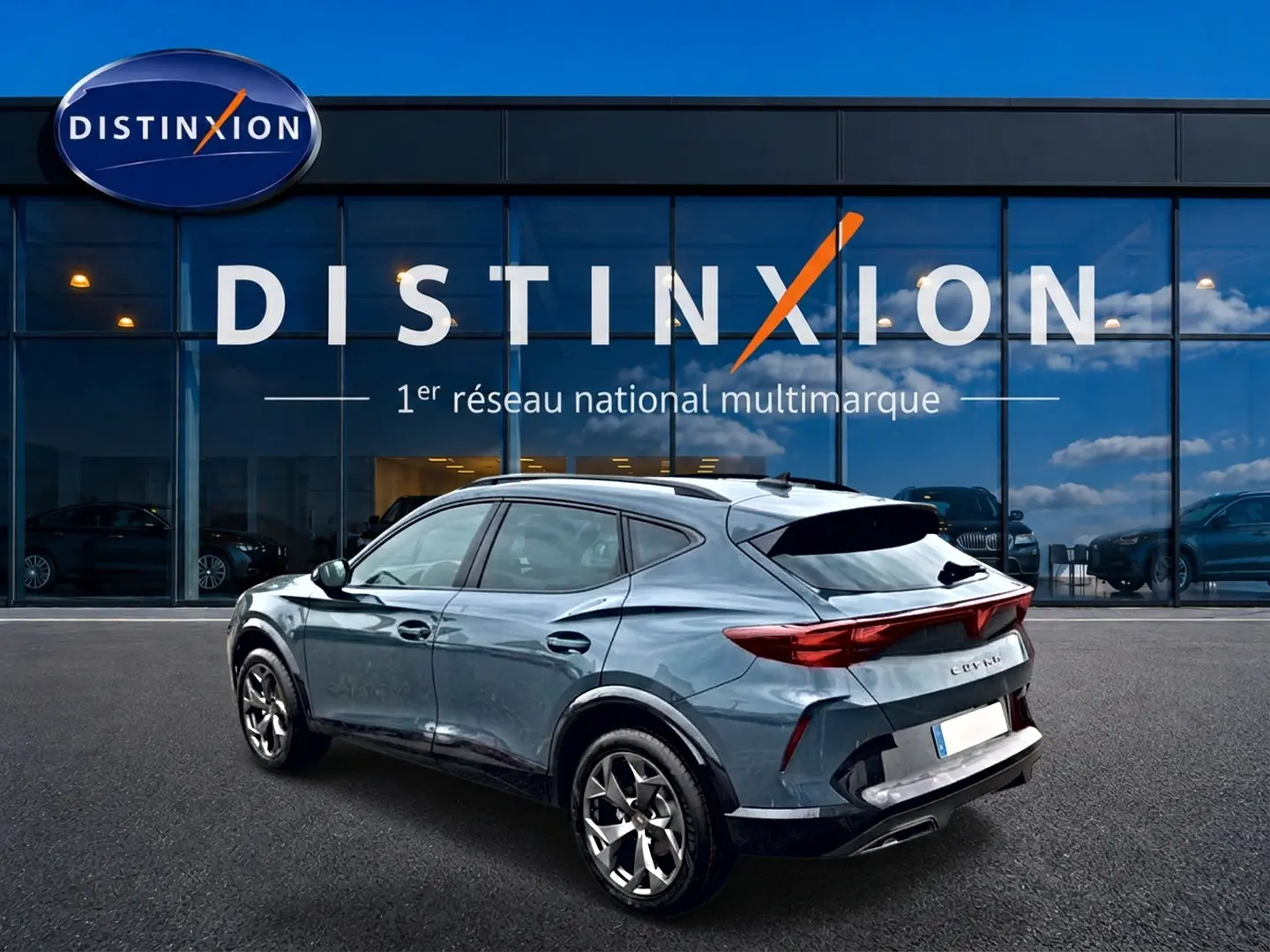 Vue 3/4 arrière droite d'un CUPRA Formentor bleu fjord avec feux arrière LED et jantes 18 pouces devant un showroom Distinxion.
