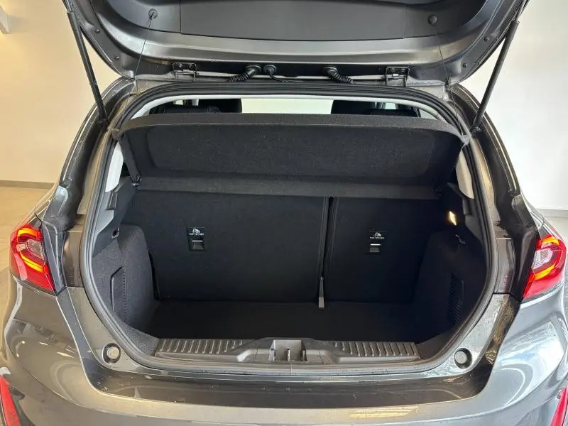 Coffre ouvert vu de l'arrière d'une Ford Fiesta 2022 gris Fashion Magnetic avec banquette rabattable et éclairage intérieur.