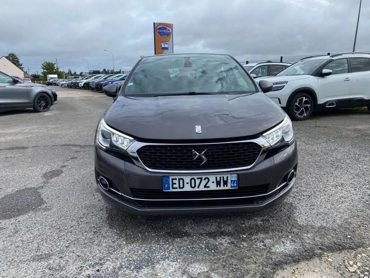 Vue avant d'une DS4 gris clair avec calandre noire et feux diurnes LED sur un parking extérieur.