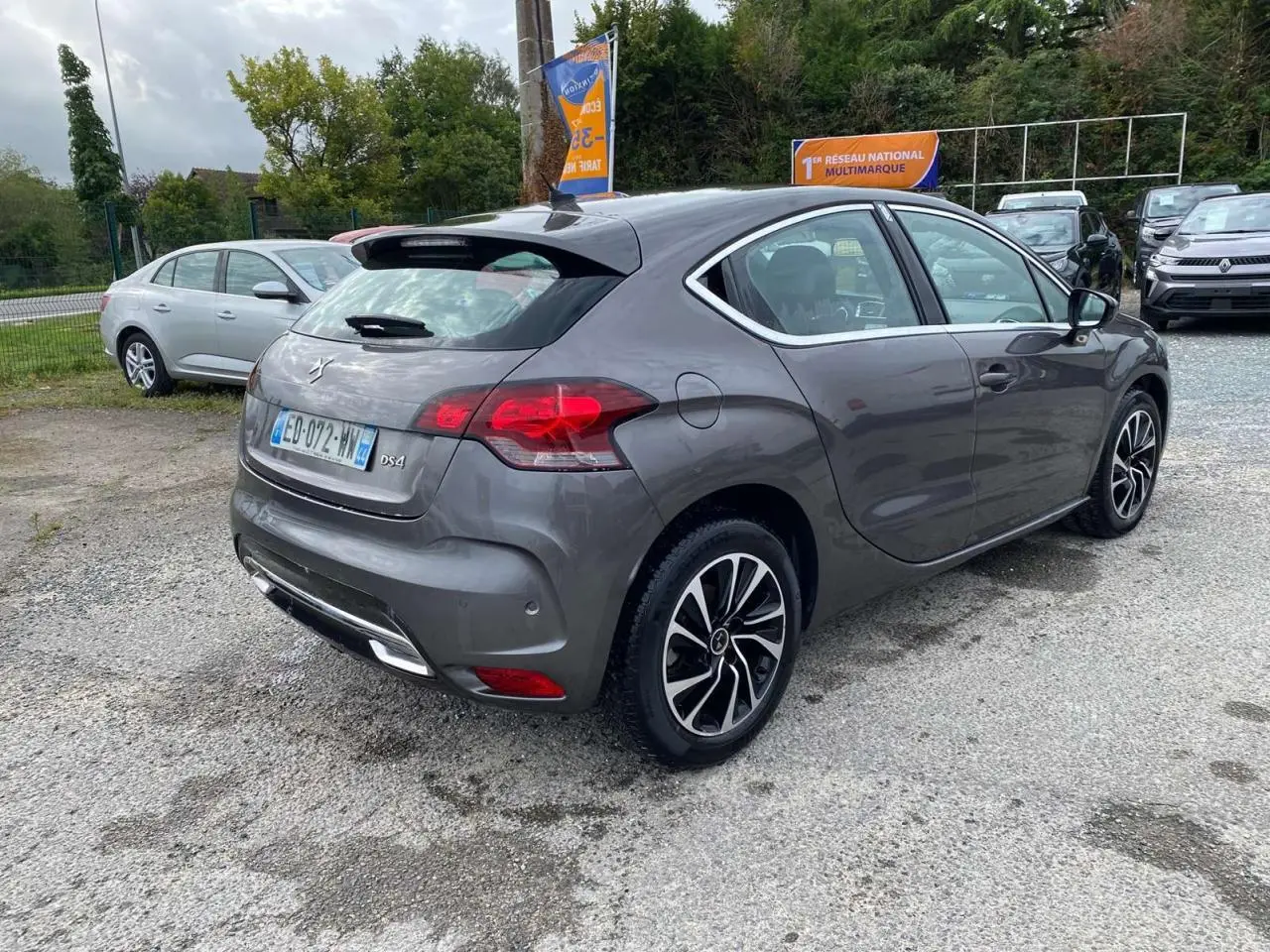 Vue 3/4 arrière droite d'une DS4 gris clair avec jantes alliage et feux arrière LED dans un parking extérieur.