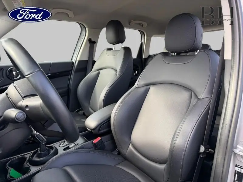 Vue intérieure côté droit des sièges avant en similicuir noir du MINI COUNTRYMAN Cooper 2023, avec accoudoir central et volant cuir.