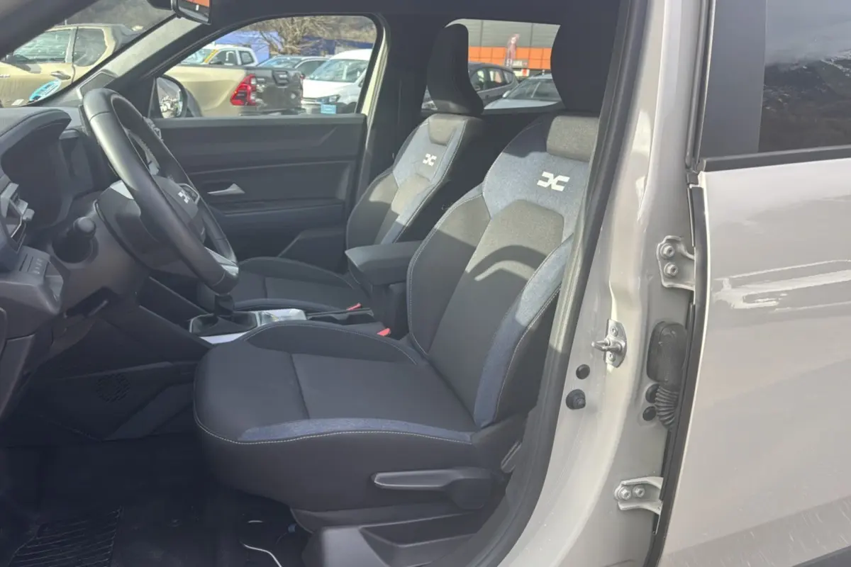 Vue intérieure côté conducteur du Dacia Duster TCE 130 4x2 Journey 2025 en couleur Sandstone, sièges tissu avec logo distinctif.