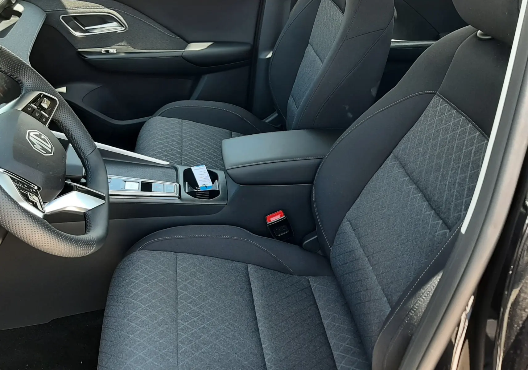 Vue intérieure côté conducteur du MG ZS 1.5L Hybrid+ 2026 avec sièges tissu gris et console centrale noire.
