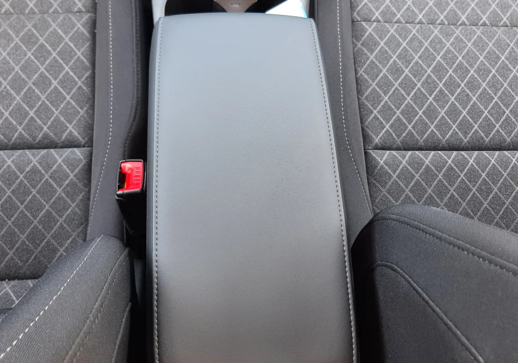 Vue plongeante sur l'accoudoir central noir et les sièges tissu gris à motifs du MG Motor ZS 1.5L Hybrid+ 2026.