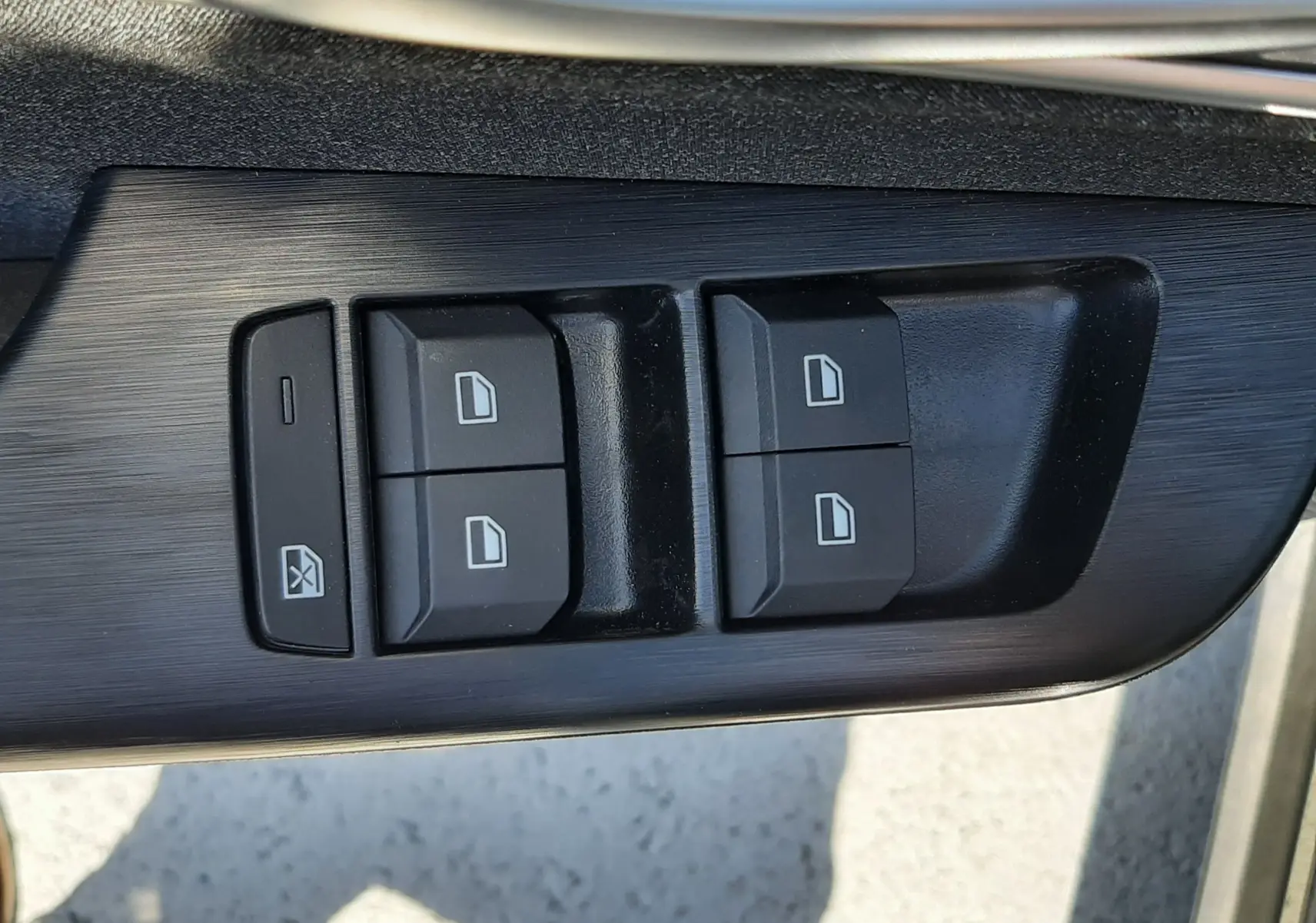 Gros plan sur les commandes de lève-vitres électriques côté conducteur du MG MOTOR ZS 1.5L Hybrid+ noir, finition intérieure noire.