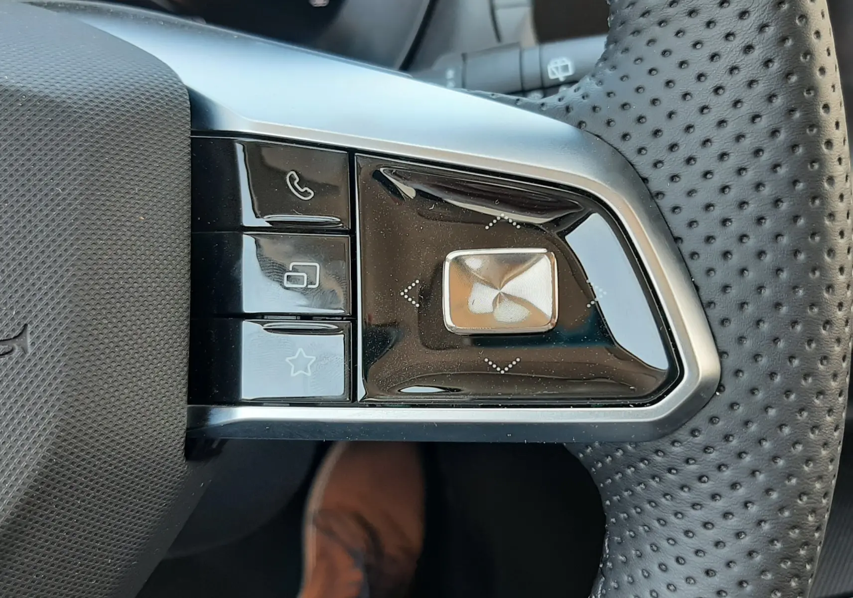 Gros plan sur les commandes noires et argentées au volant perforé du MG MOTOR ZS hybride, côté gauche.