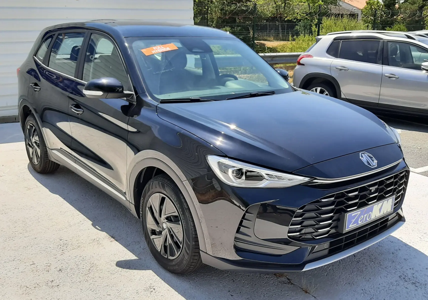 Vue 3/4 avant d’un MG ZS 1.5L Hybrid+ 197ch noir Pebble Black Metal avec calandre imposante et jantes aérodynamiques.