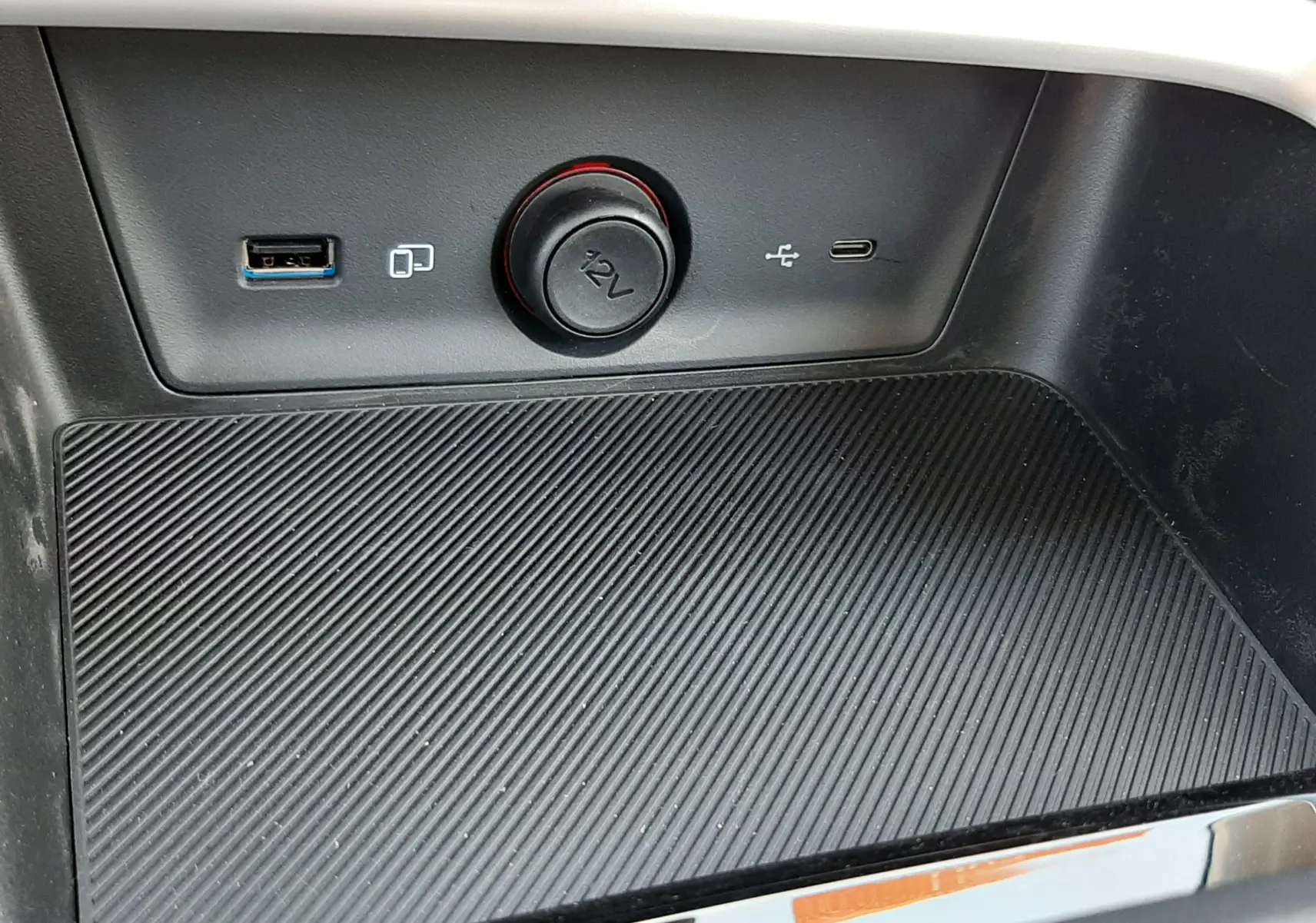 Gros plan sur la console centrale du MG MOTOR ZS 1.5L HYBRID+ 197CH avec prises USB et allume-cigare 12V, surface antidérapante.
