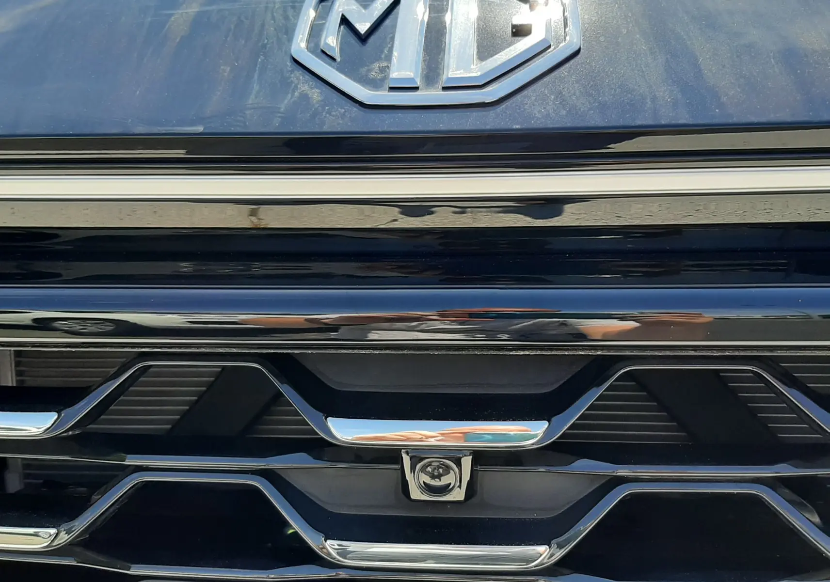 Gros plan sur la calandre noire Pebble Black Metal du MG ZS 1.5L Hybrid+ 197ch avec logo MG chromé et détails chromés.