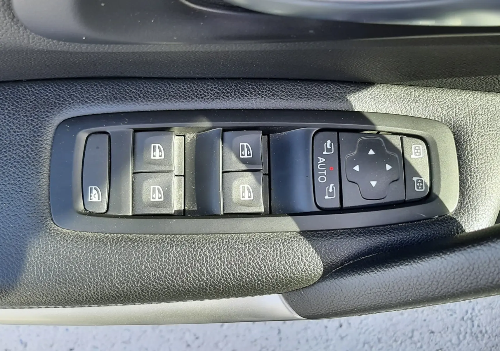 Gros plan sur les commandes des vitres électriques et rétroviseurs sur la porte côté gauche d’un Renault Kadjar gris titanium.
