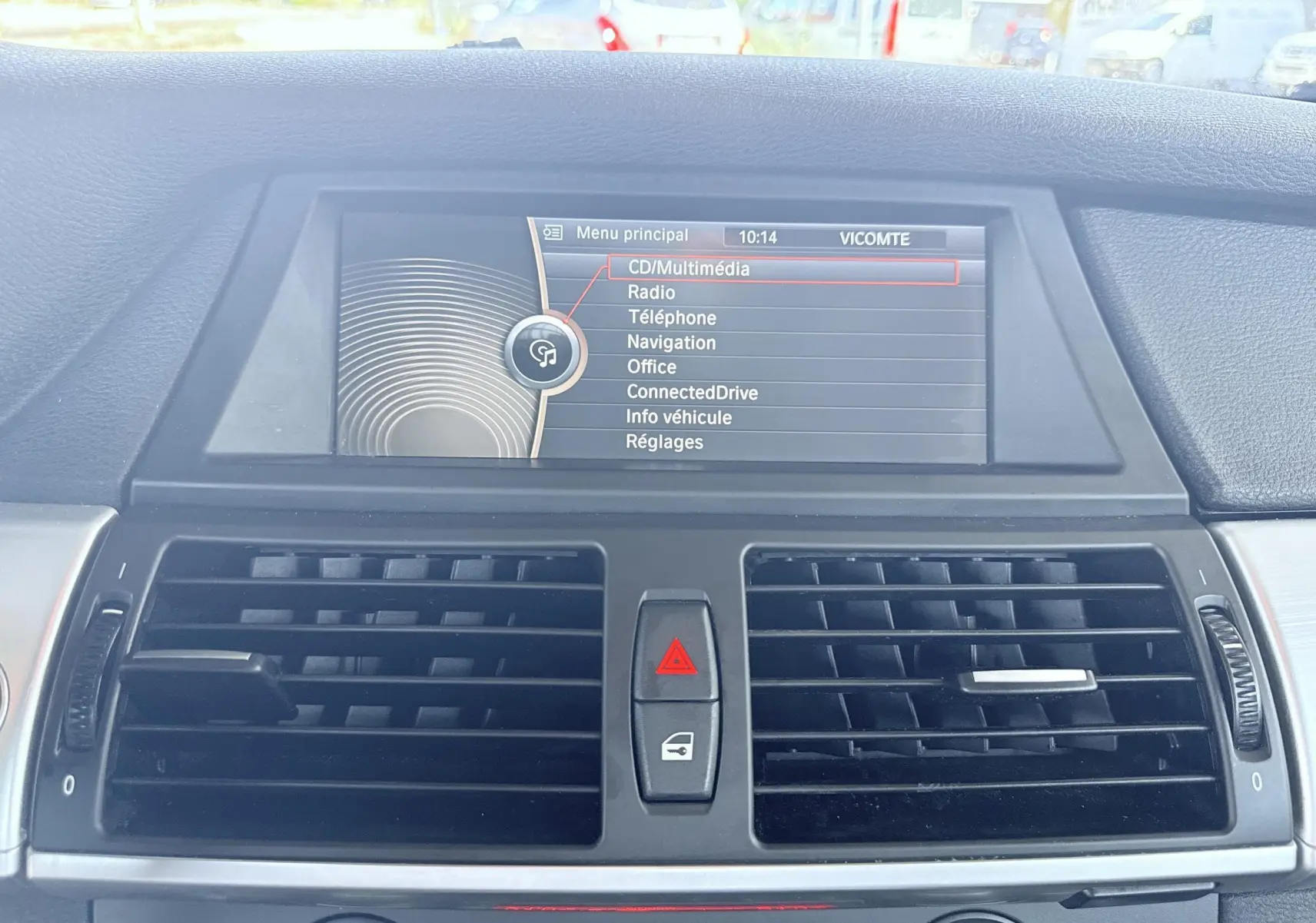Vue intérieure du tableau de bord de la BMW X6 2011, écran central affichant le menu multimédia, avec aérateurs noirs.