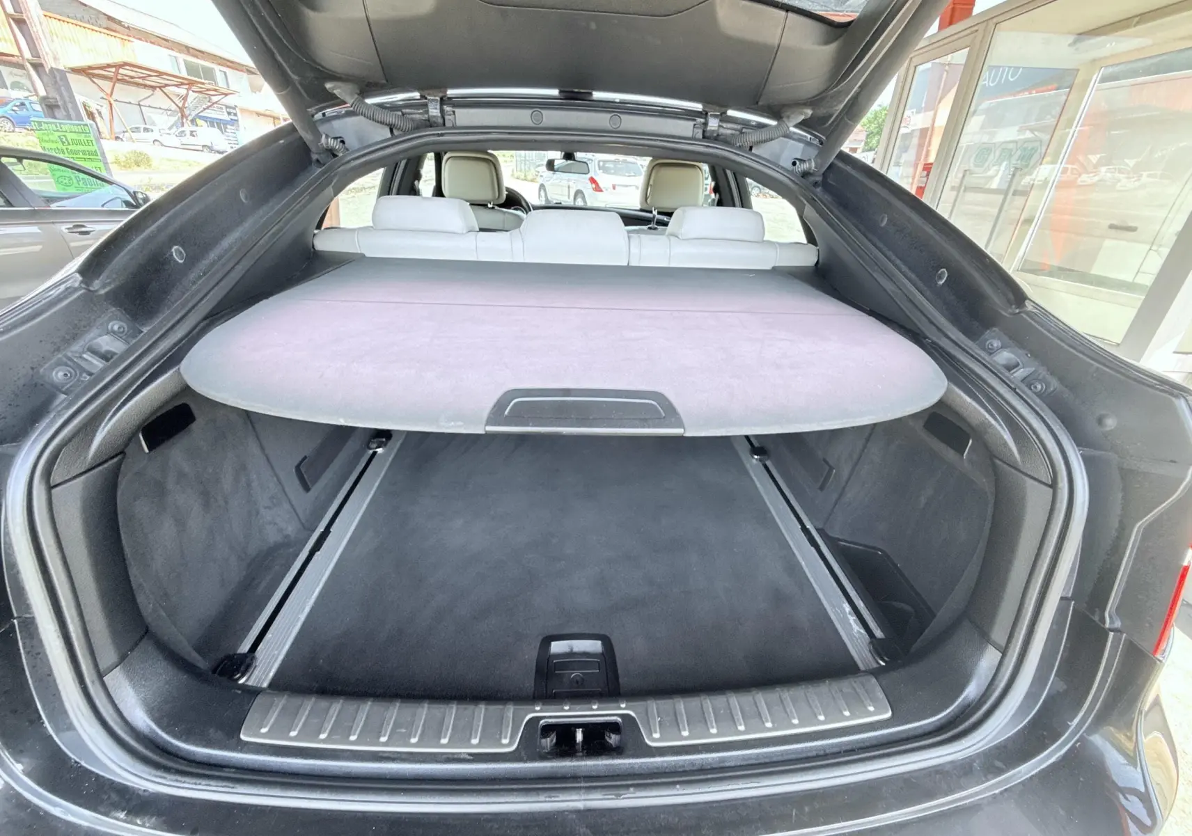 Coffre ouvert vu de l’arrière d’un BMW X6 noir, avec cache-bagages et sièges arrière en cuir clair visibles.