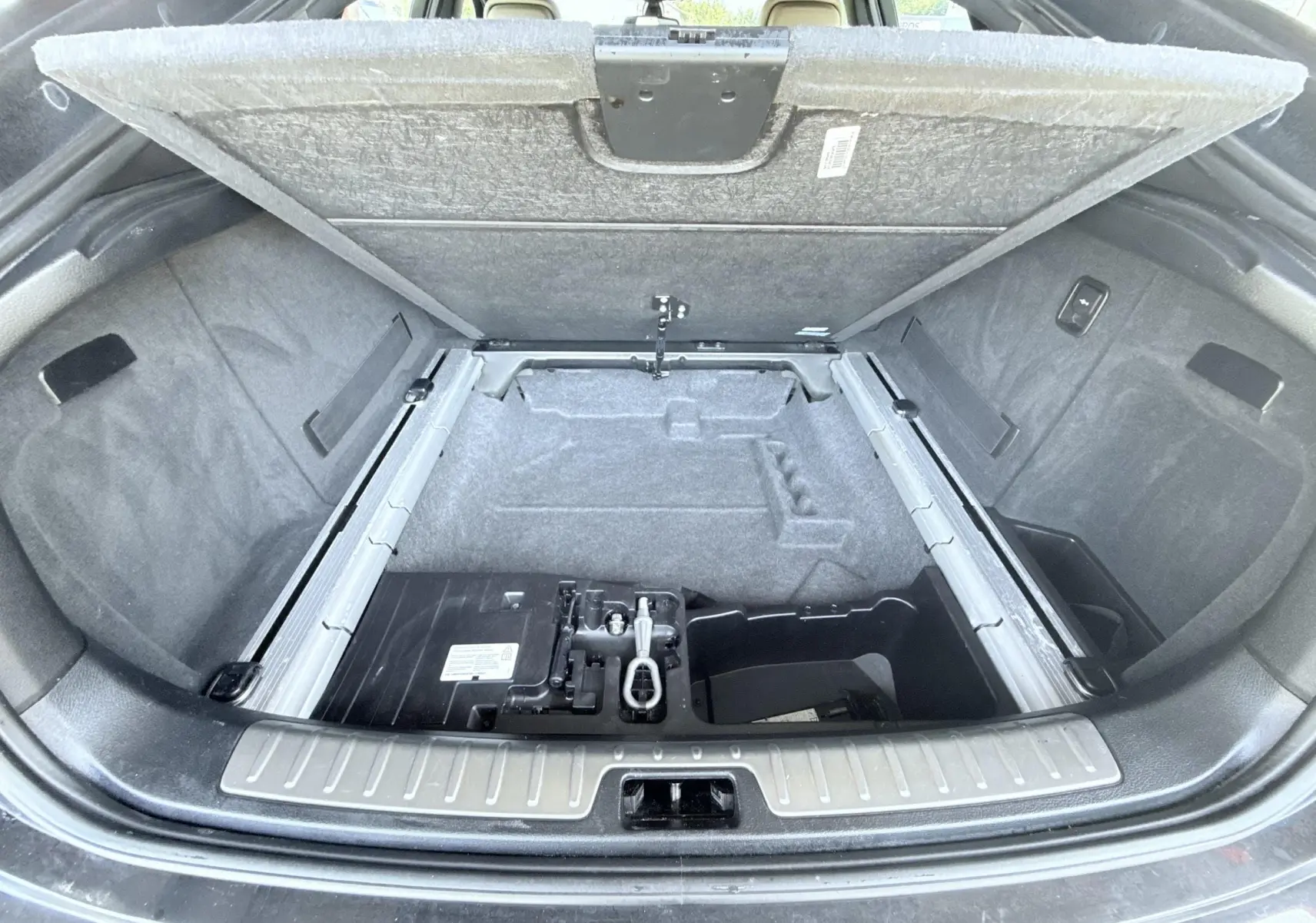 Coffre ouvert vu de l'arrière d'un BMW X6 noir, montrant le compartiment de rangement sous le plancher.