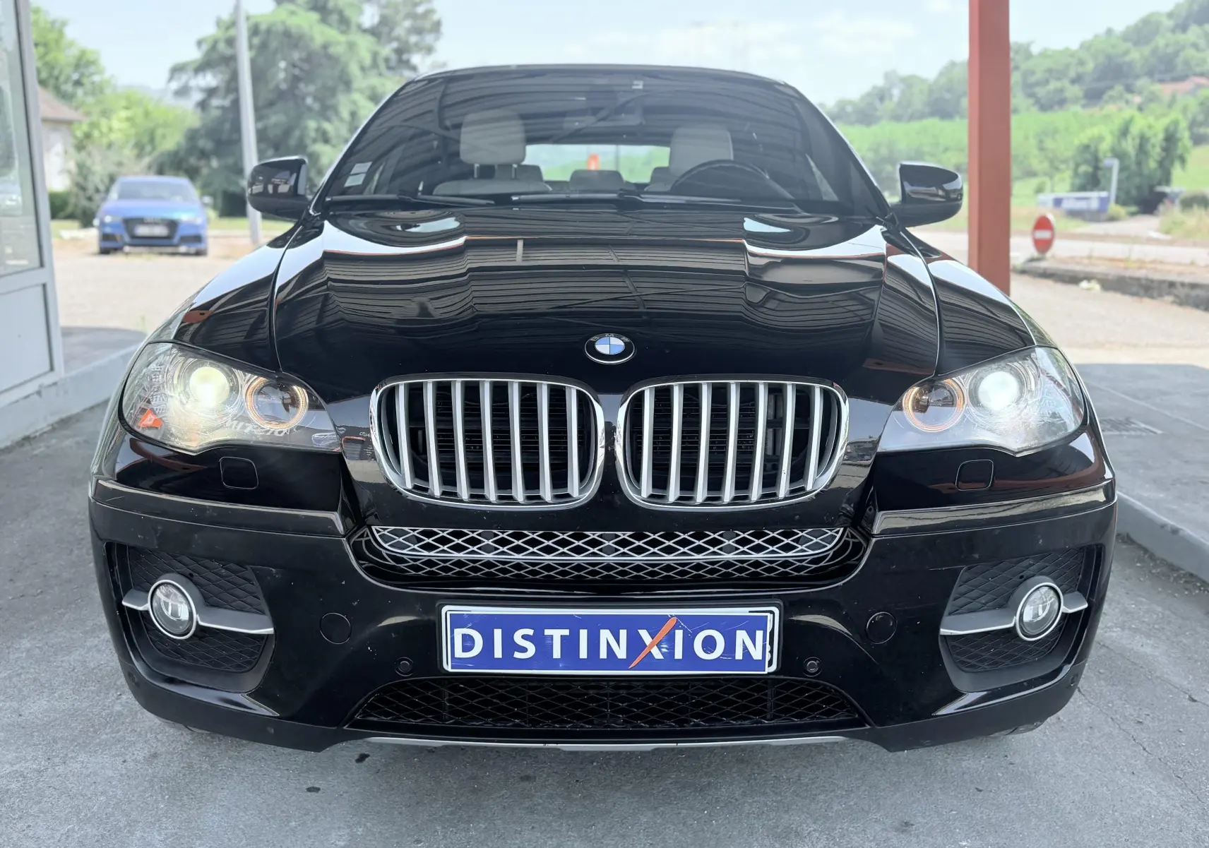 Vue frontale d’un BMW X6 noir avec phares allumés et calandre chromée sous un abri extérieur.