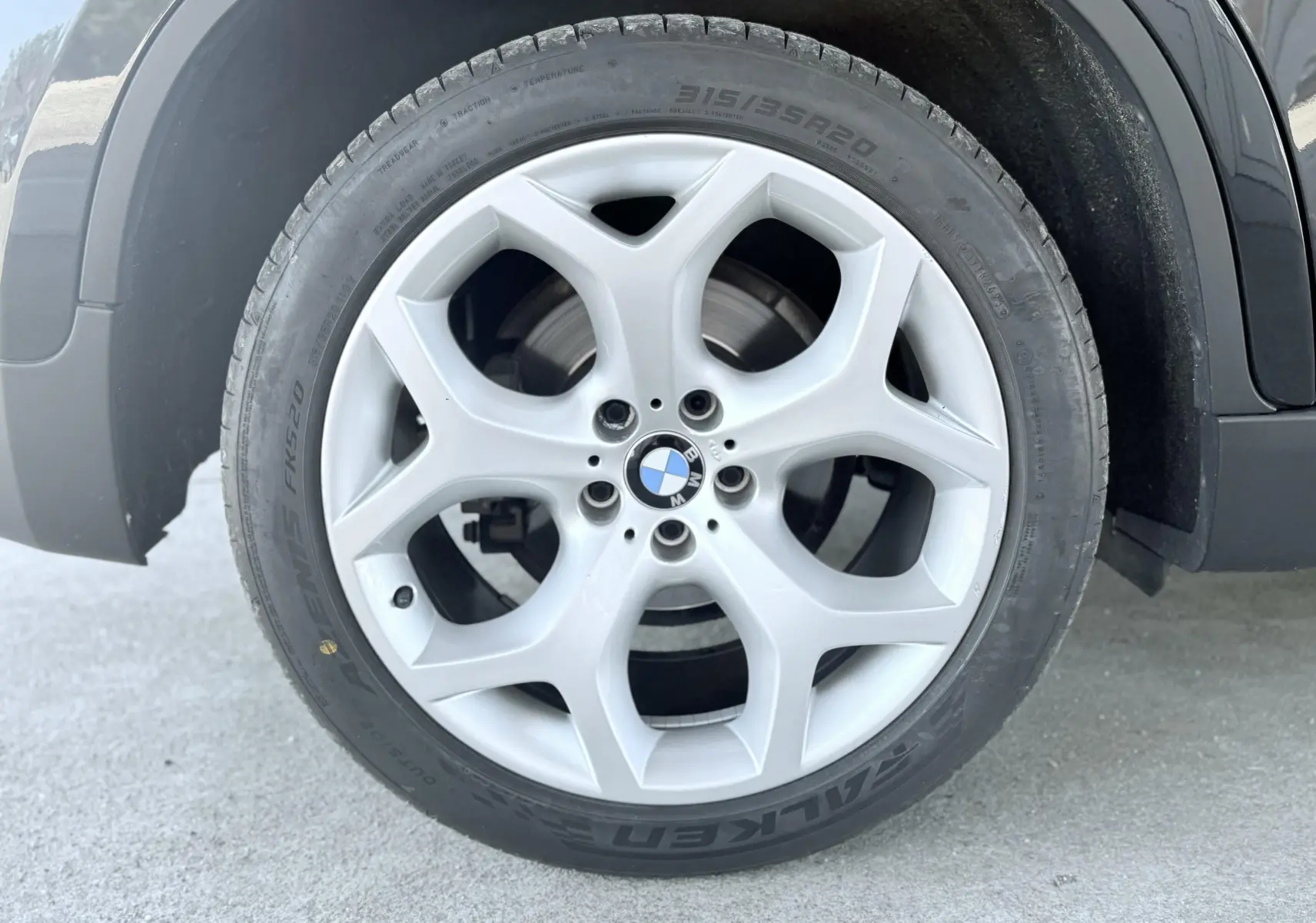 Gros plan sur la roue avant droite noire d’un BMW X6 2011 avec jante alliage argentée à cinq branches.