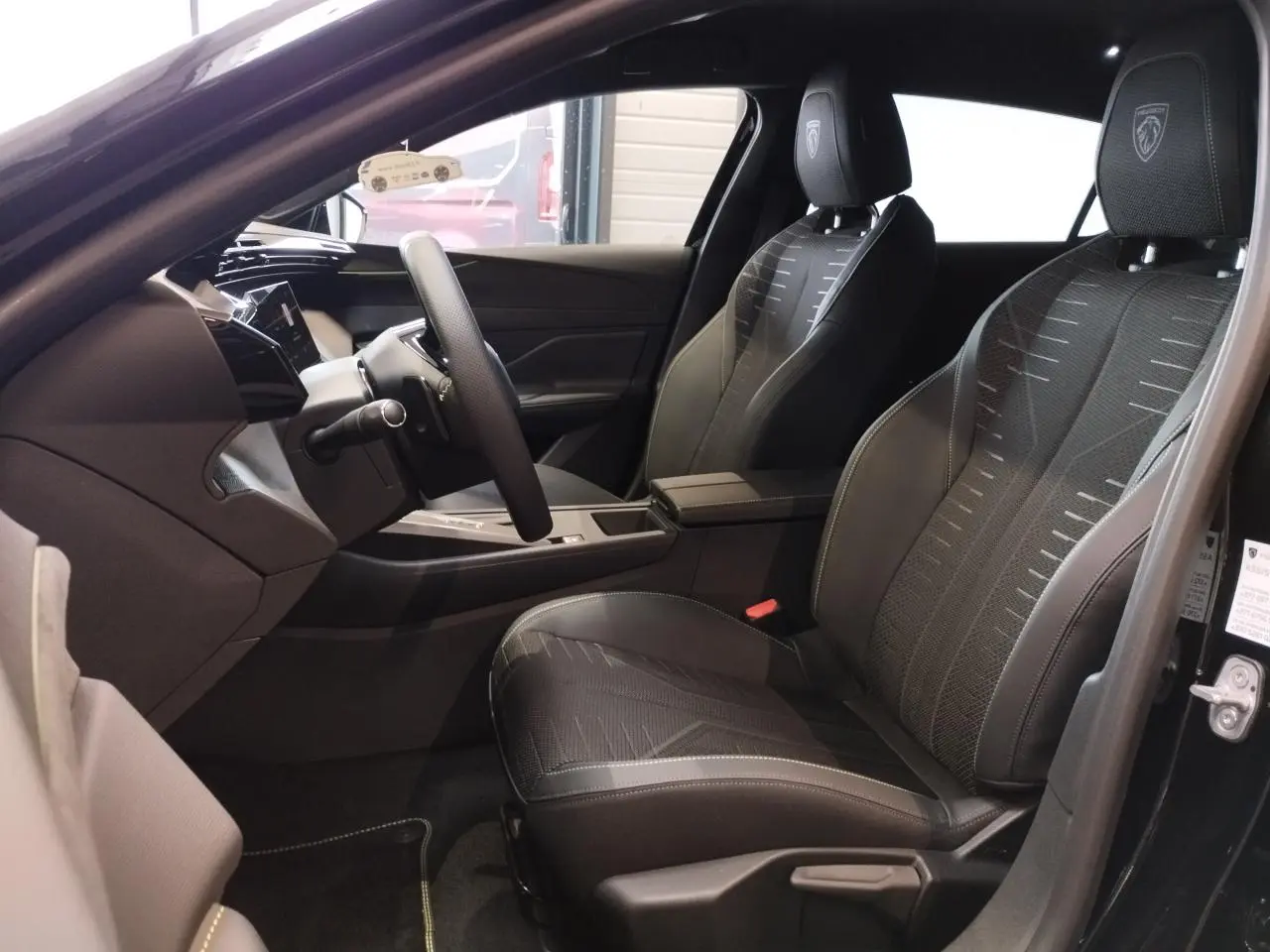 Vue intérieure côté conducteur de la Peugeot 308 hybride 2026 noire, sièges tissu noir avec surpiqûres vert Adamite.
