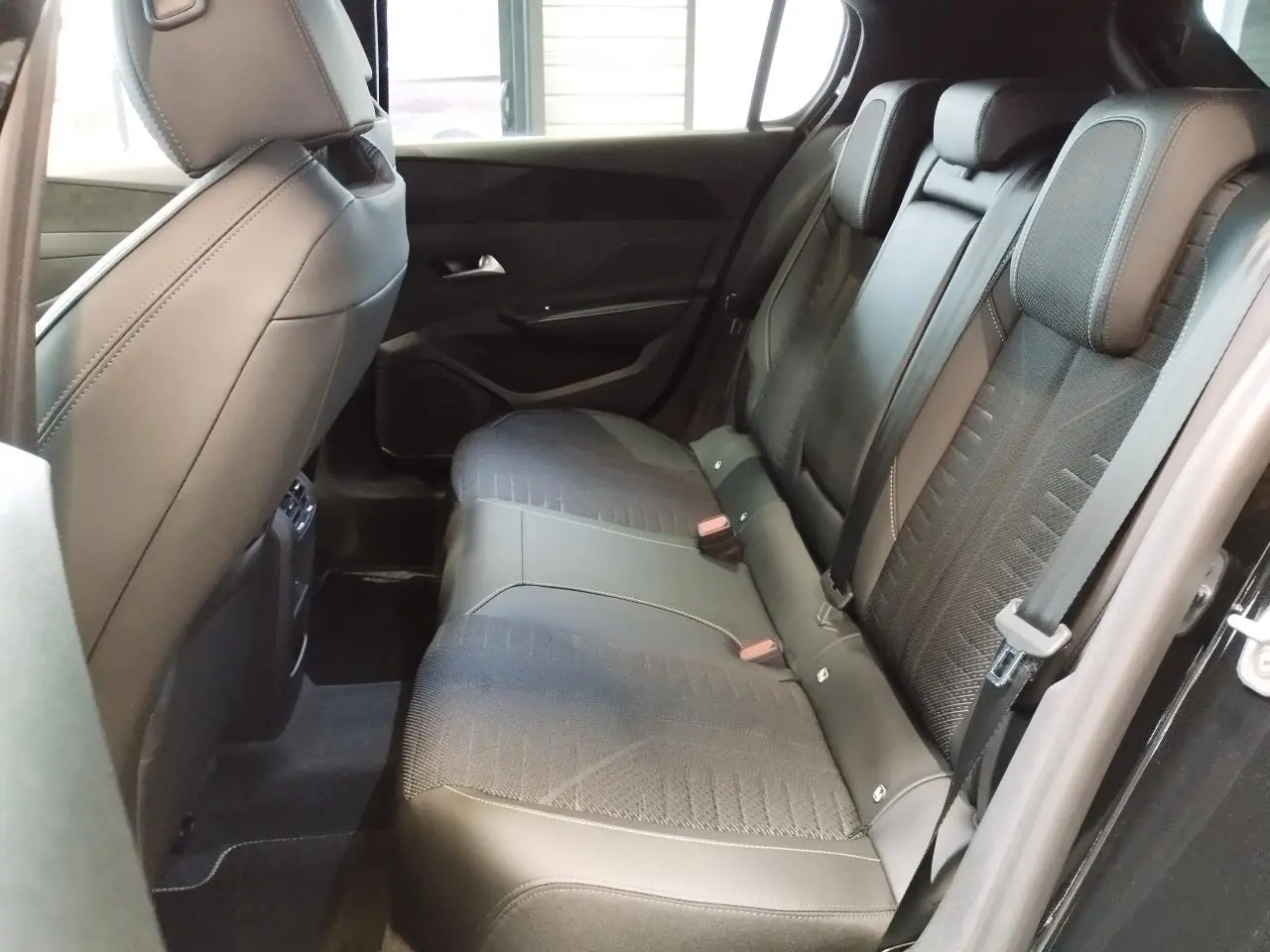 Vue intérieure côté droit montrant la banquette arrière noire avec surpiqûres vert Adamite sur Peugeot 308 Hybrid 2026.