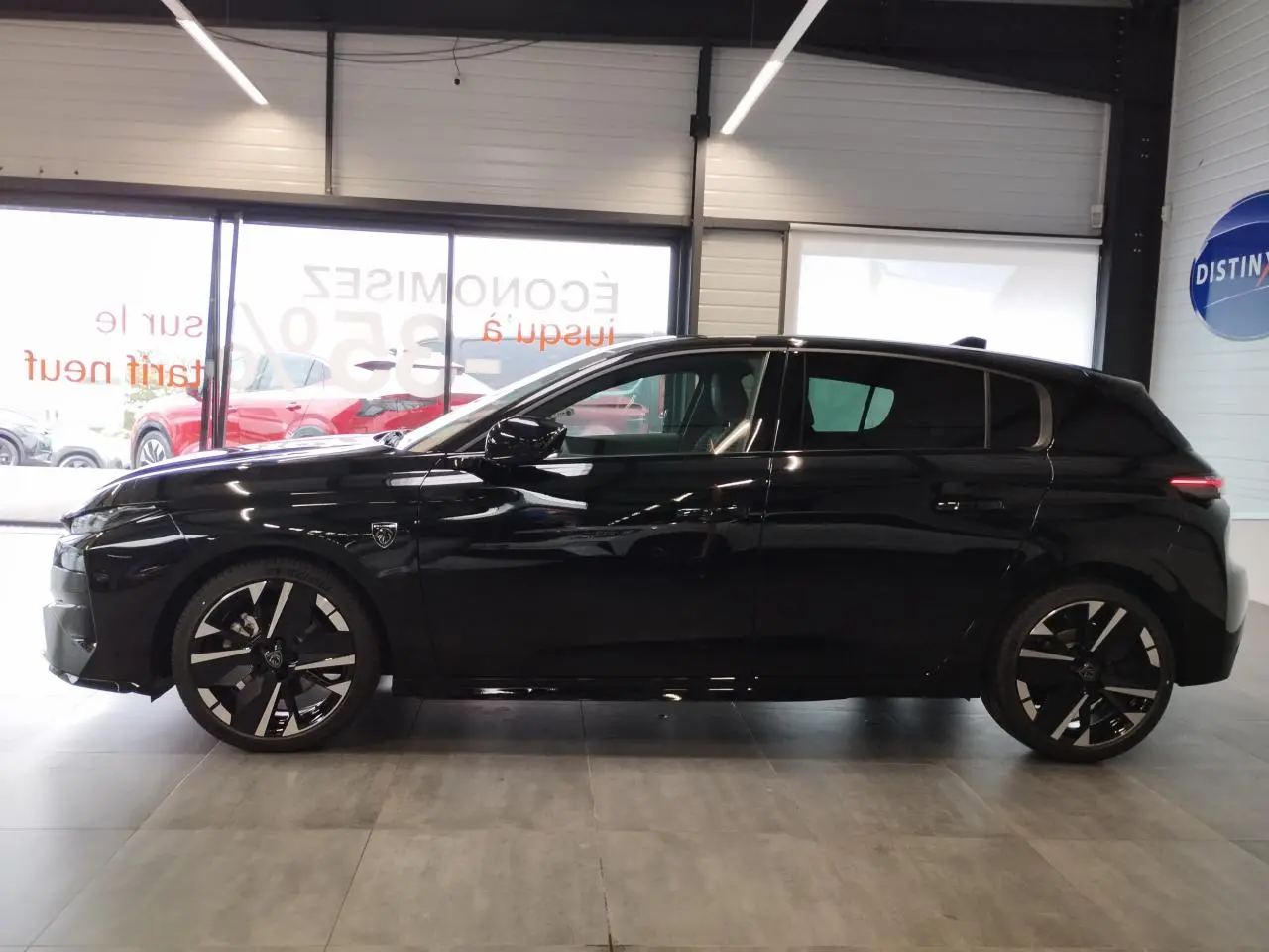 Peugeot 308 1.2i Hybrid noire métallisée vue de profil côté gauche, avec jantes alliage bi-ton et blason sur aile avant.