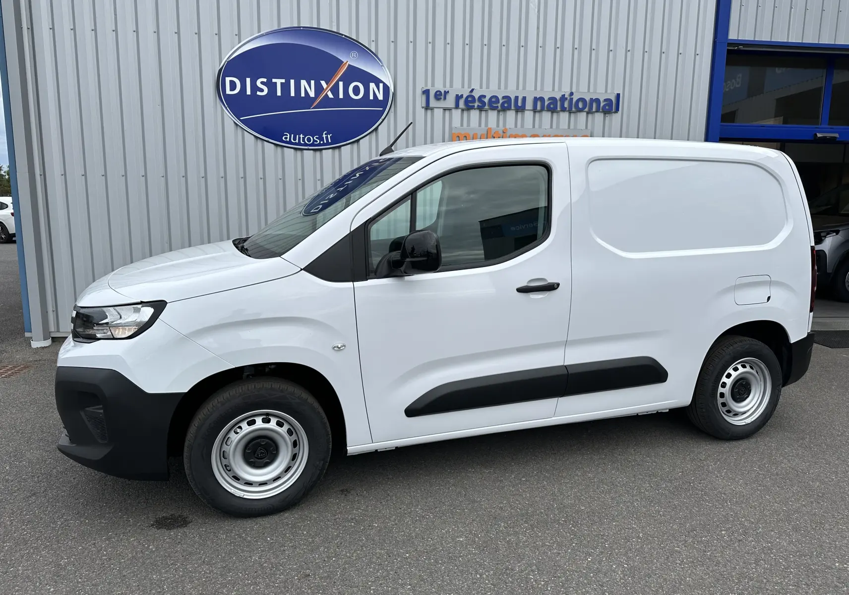 Peugeot Partner Fourgon blanc vu de profil côté gauche, avec protections noires sur les portières et roues acier.