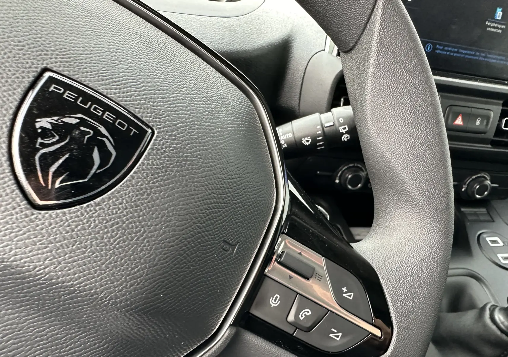 Gros plan sur le volant en cuir noir du Peugeot Partner Fourgon 2024 avec commandes intégrées et logo lion argenté.