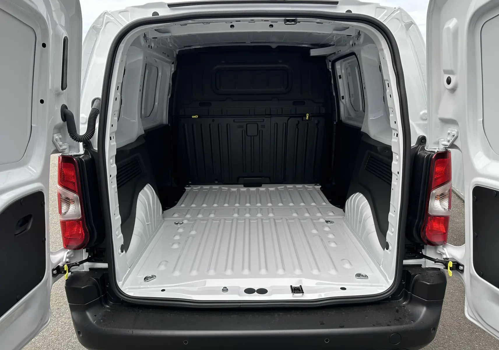 Vue arrière ouverte du fourgon blanc Peugeot Partner BlueHDi 100ch M 2024, montrant l'espace de chargement vide et spacieux.