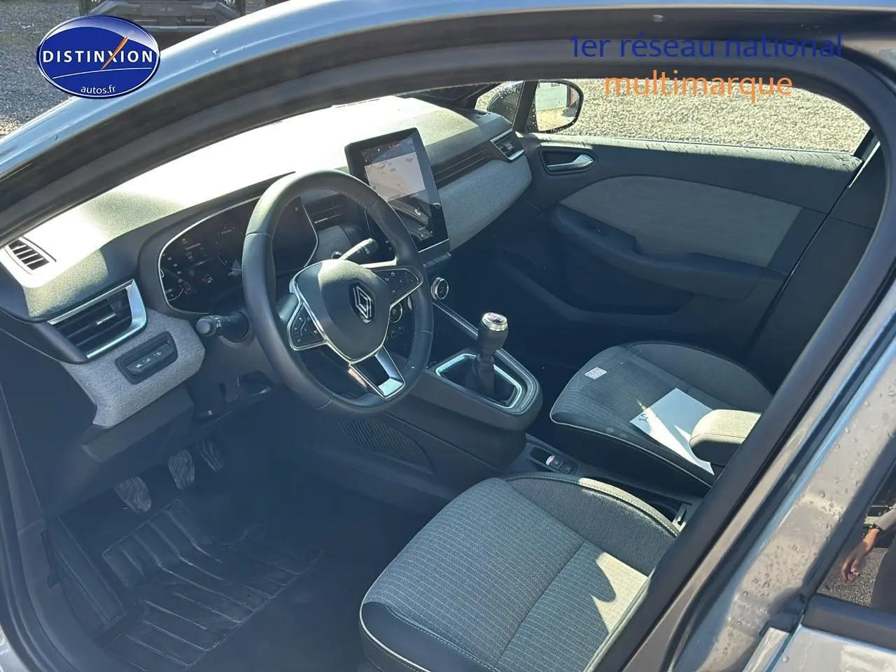 Intérieur de la Renault Clio V gris pizarra vu côté conducteur, volant textile et levier de vitesses manuel visibles.