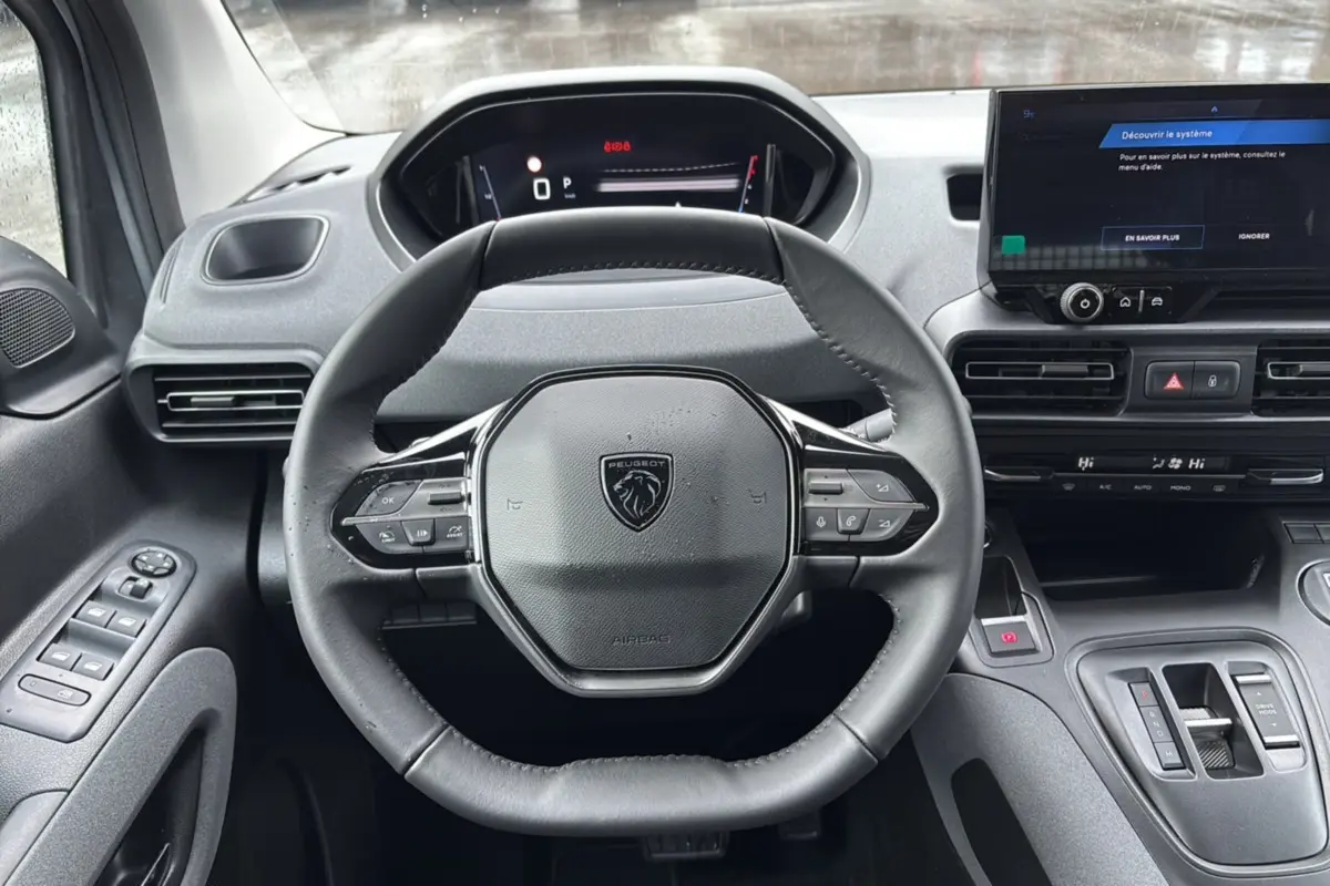 Vue rapprochée du volant cuir multifonctions et du tableau de bord numérique du Peugeot Rifter gris Artense 2026.