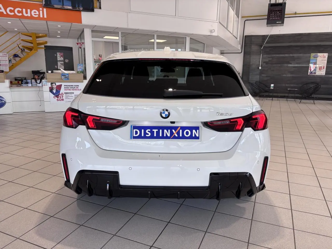 Vue arrière d'une BMW Série 1 120d M Sport blanche de 2025 avec feux LED et diffuseur noir en concession.