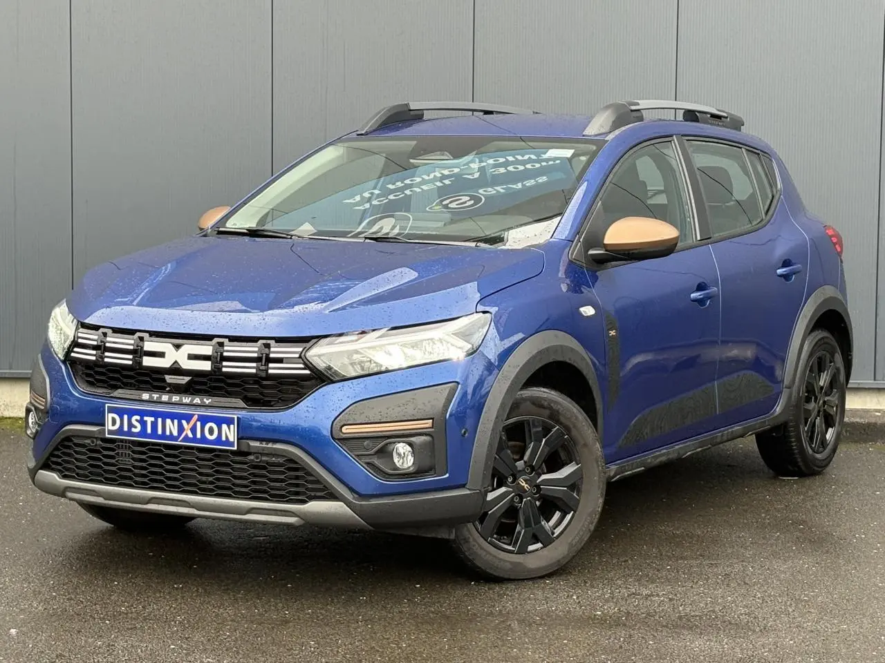Vue 3/4 avant droite d'une Dacia Sandero Stepway Bleu Iron avec jantes noires et coques de rétroviseurs cuivrées.