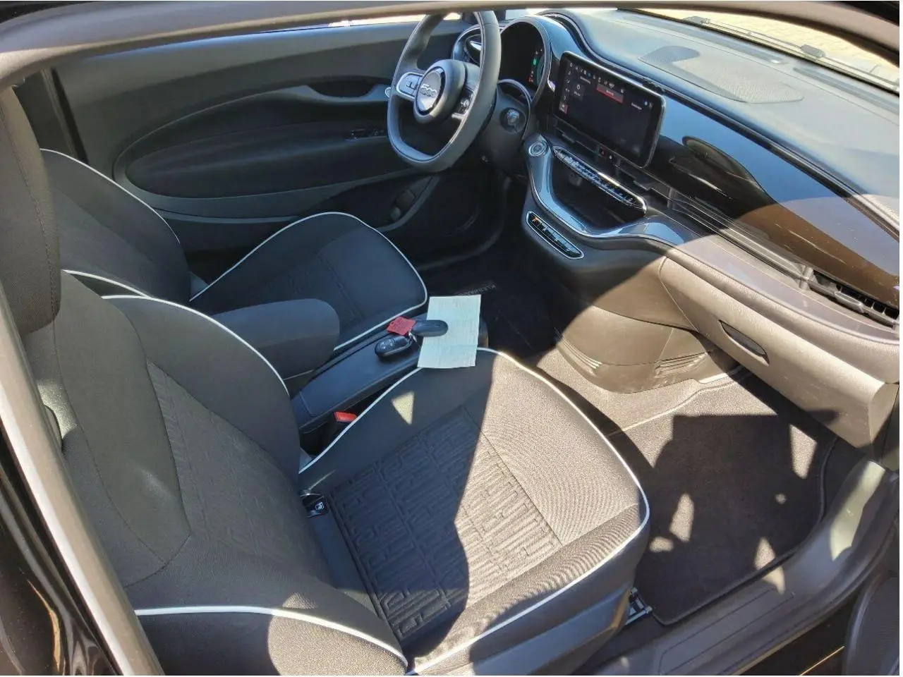 Vue intérieure côté conducteur de la Fiat 500 électrique 2024 avec sellerie tissu noir et écran tactile central.