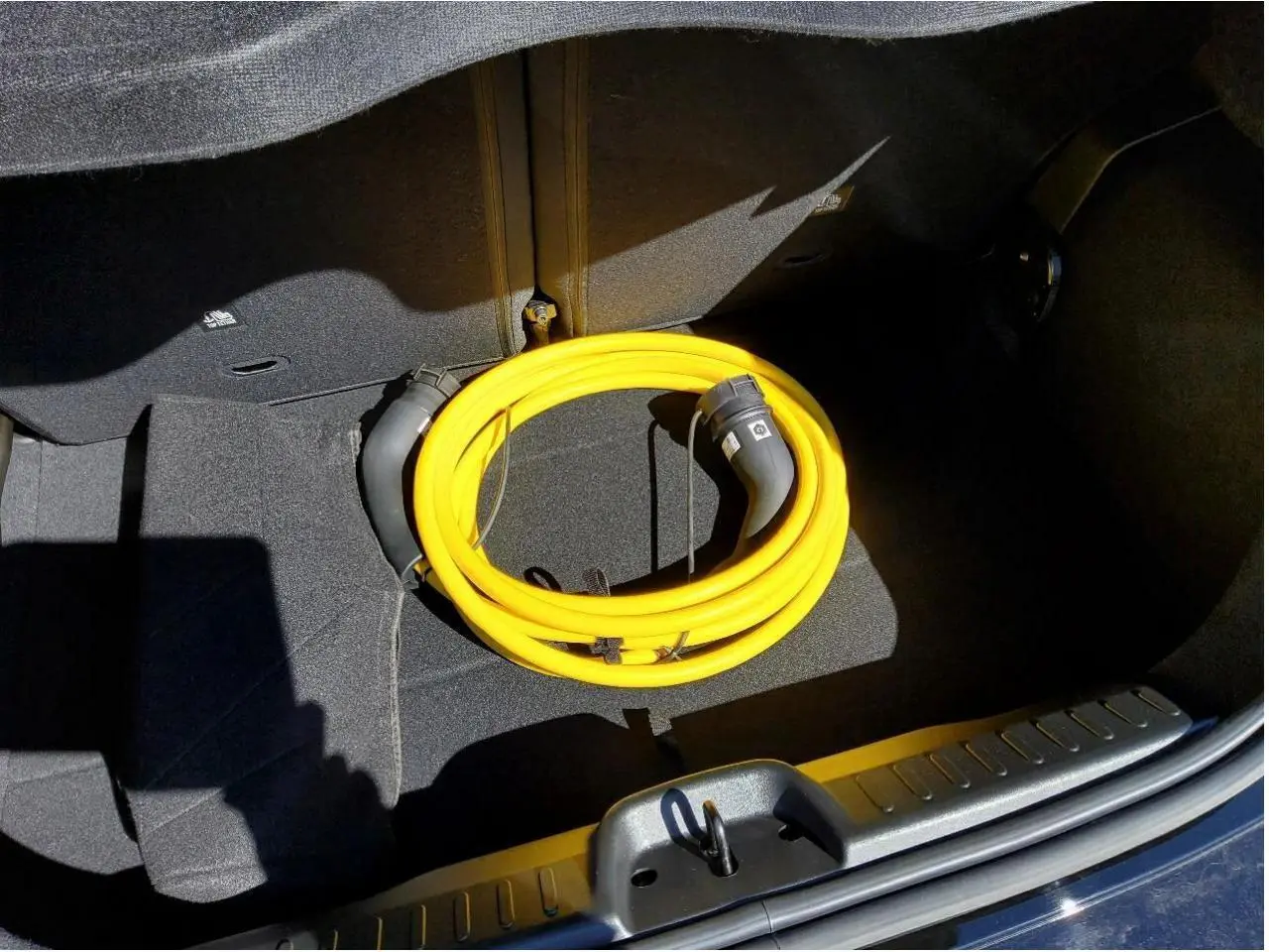 Coffre ouvert d'une FIAT 500 électrique noire avec câble de recharge jaune enroulé visible au centre.