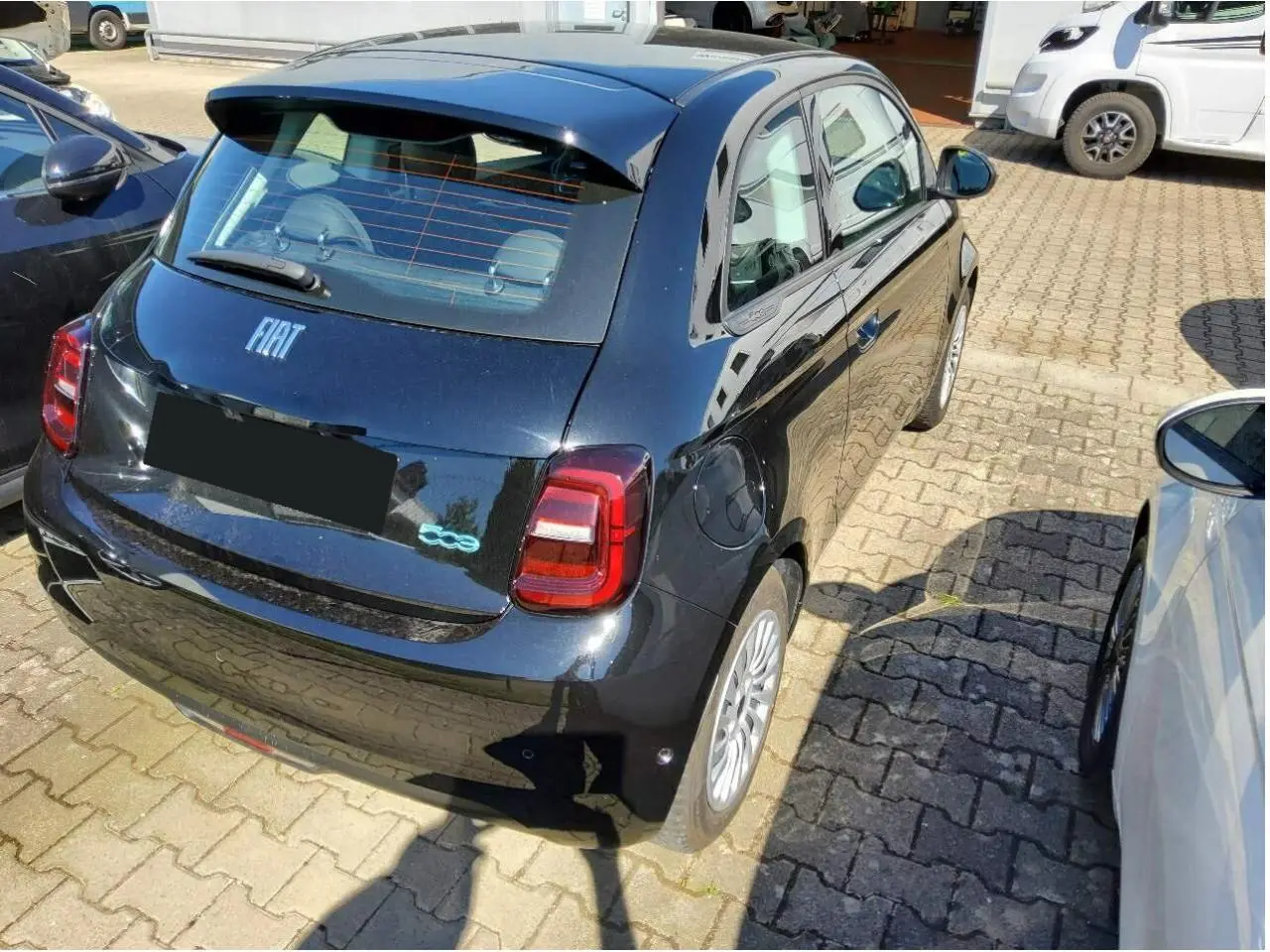 Vue 3/4 arrière droite d'une Fiat 500 électrique noire 2024 avec logo 500 bleu et feux arrière LED.