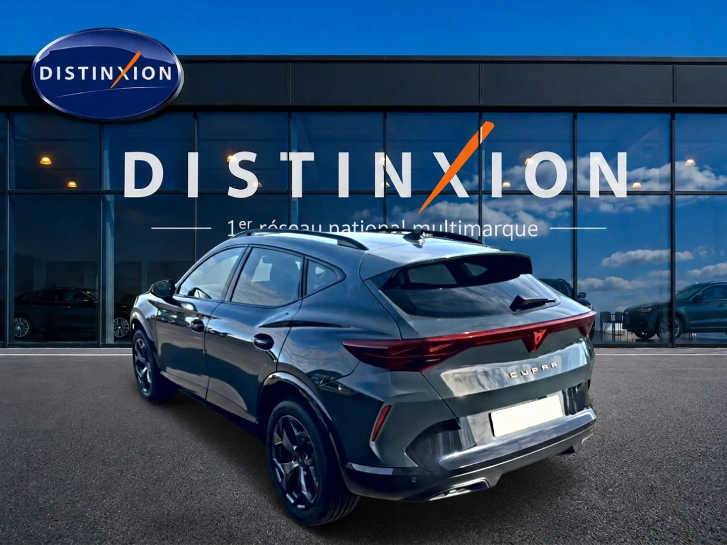 Vue 3/4 arrière droite d'un CUPRA Formentor bleu fjord avec feux arrière LED et jantes 18 pouces devant un showroom Distinxion.