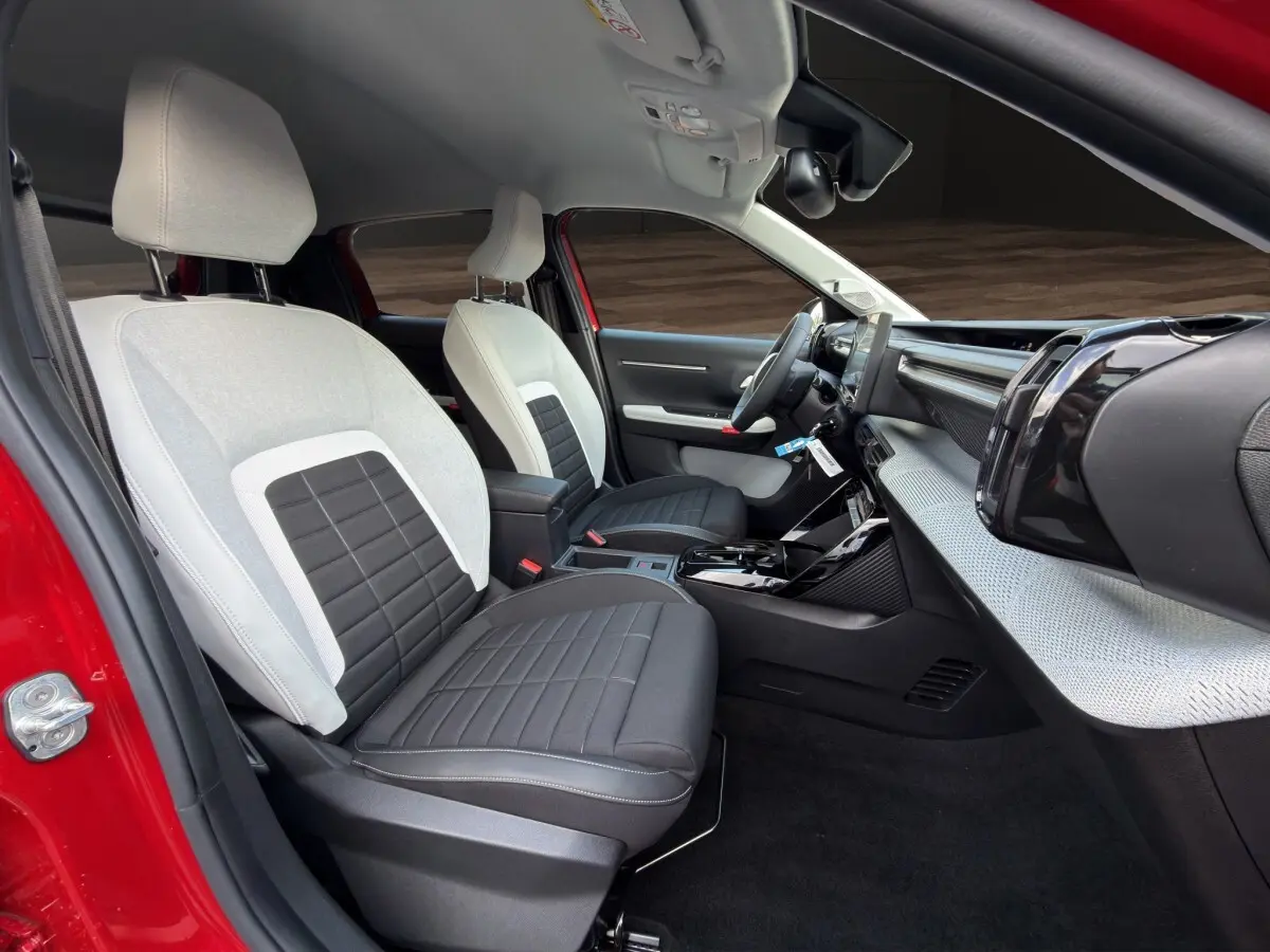 Vue intérieure côté conducteur de la Citroën C3 rouge 2026, sièges bicolores gris et noir, tableau de bord moderne avec écran tactile.