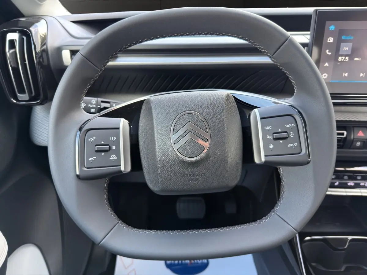 Vue rapprochée du volant cuir multifonctions de la Citroën C3 Hybride 110 MAX avec tableau de bord et écran tactile visible.