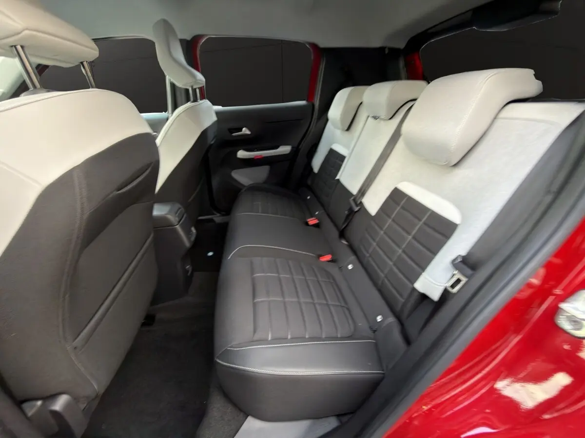 Vue intérieure arrière côté droit de la Citroën C3 hybride rouge, montrant la banquette bicolore noire et beige.