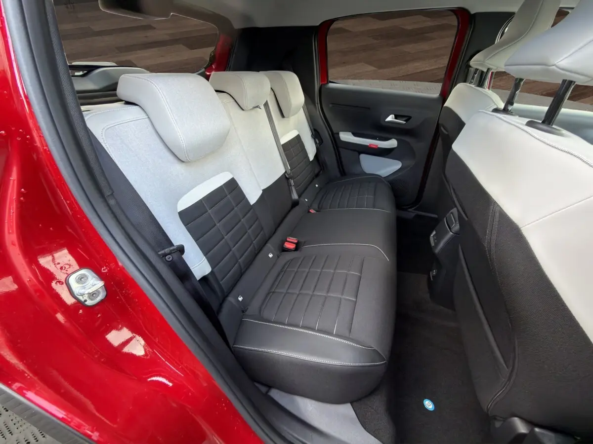 Vue intérieure arrière côté gauche de la Citroën C3 rouge 2026, banquette bicolore noire et grise avec appuie-têtes.