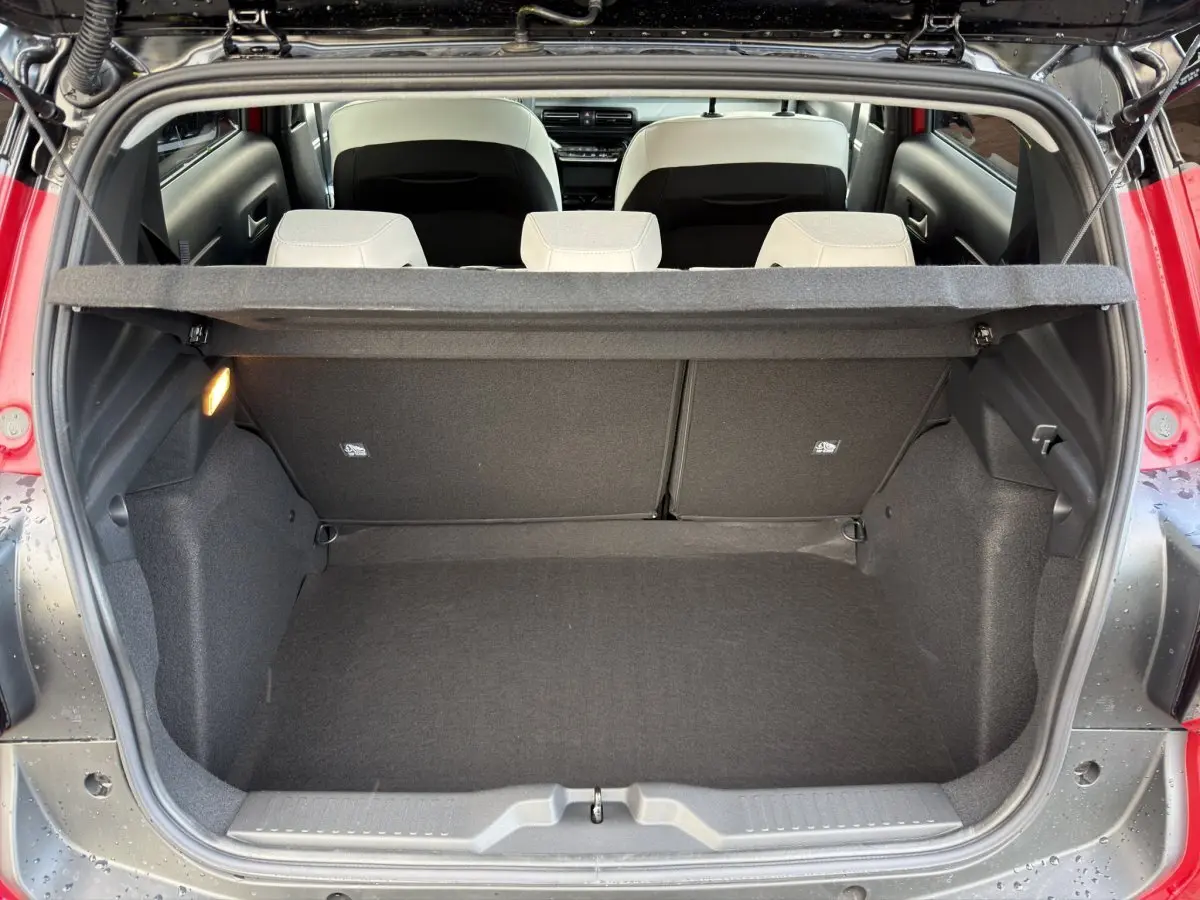 Vue arrière du coffre ouvert d'une Citroën C3 rouge hybride 2026, avec banquette arrière beige et tablette de coffre.