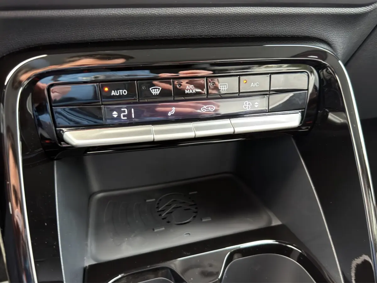 Gros plan sur la console centrale noire de la Citroën C3 hybride rouge, avec commandes climatisation et zone de recharge par induction.