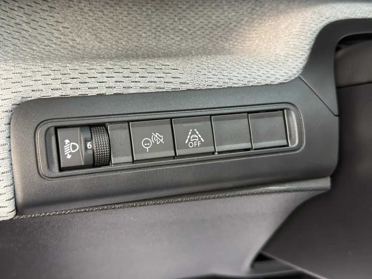 Gros plan sur les commandes de réglage des phares et d'aide à la conduite dans une Citroën C3 hybride rouge.
