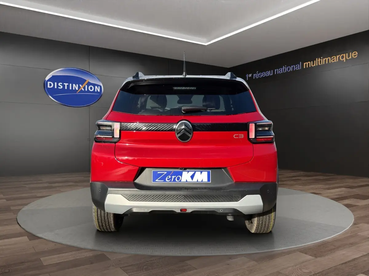 Vue arrière d'une Citroën C3 rouge 2026 avec logo noir et bande noire distinctive sous la lunette arrière.