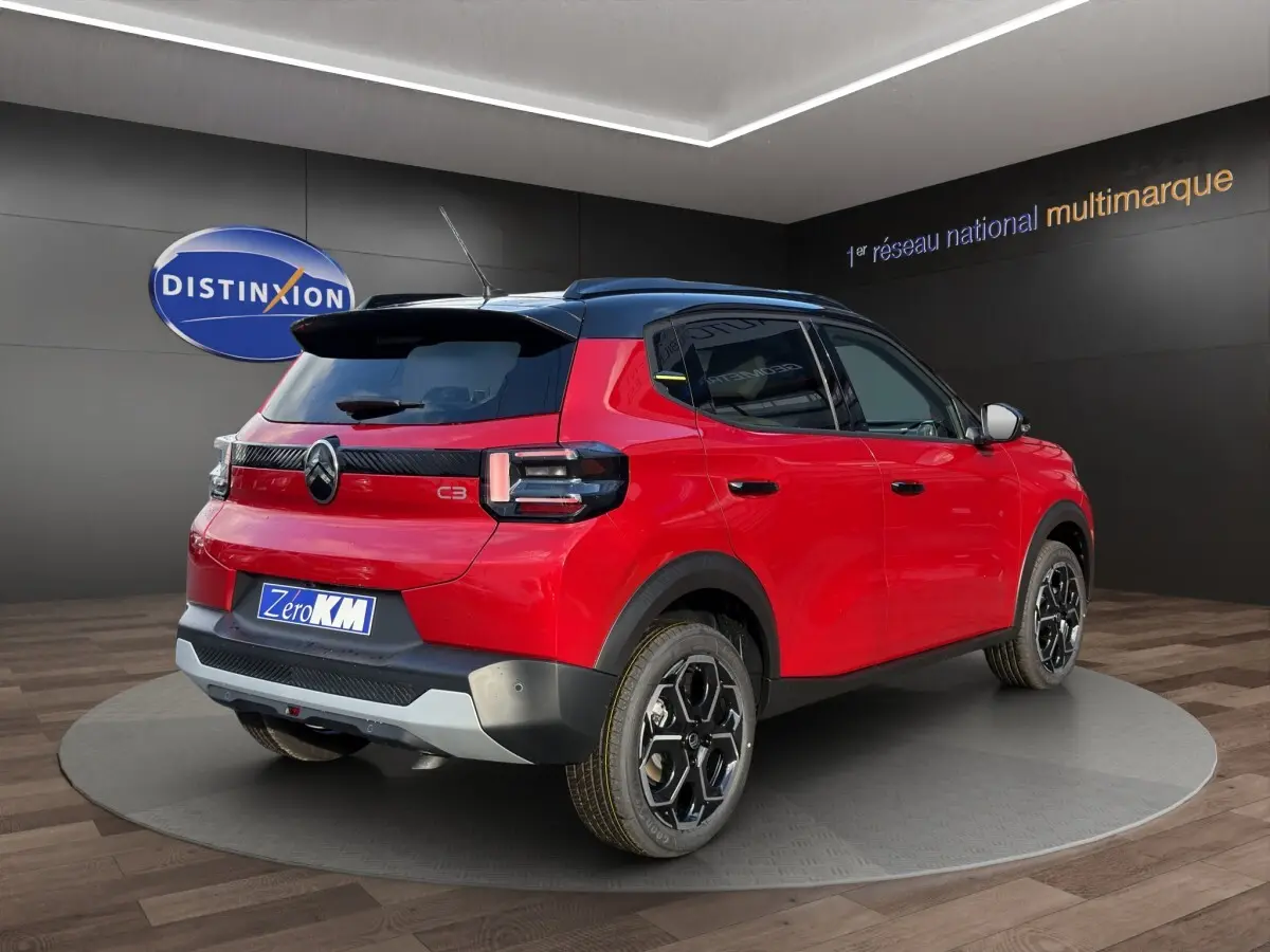 Vue 3/4 arrière droite d'une Citroën C3 hybride rouge avec toit noir et jantes noires distinctives.