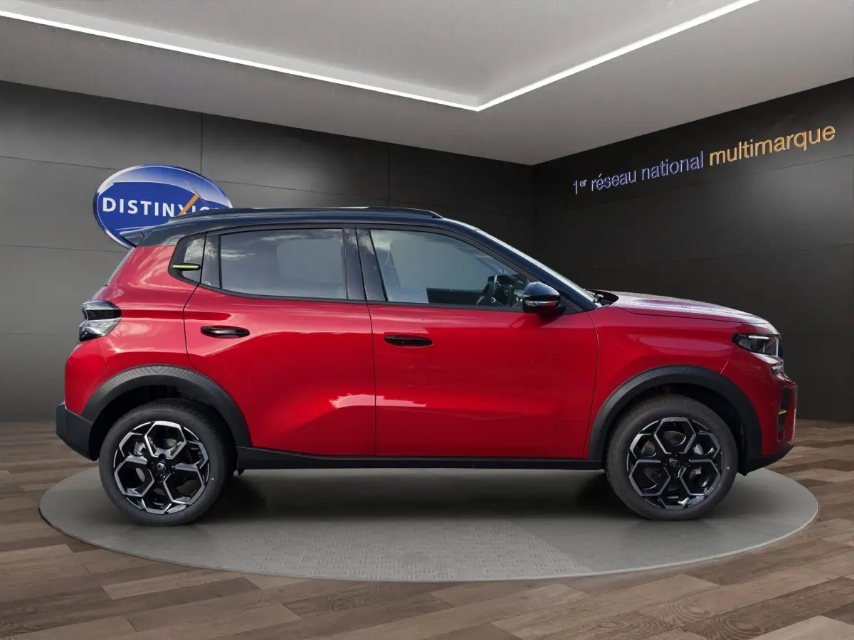 Profil côté gauche d'un Citroën C3 hybride rouge avec toit noir et jantes alliage au design hexagonal.