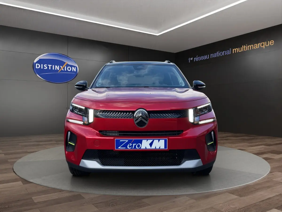 Vue avant d'une Citroën C3 hybride rouge avec phares LED et calandre noire brillante en showroom.