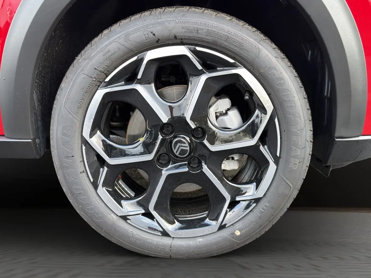 Gros plan sur la roue avant droite d’une Citroën C3 rouge avec jante alliage noire et argentée au design hexagonal.